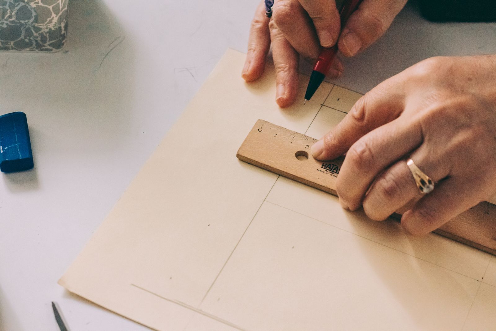 Hands measuring an architectural drawing with a ruler and pencil